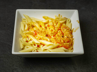 Cooked pasta dish with cheese sauce and herbs in white square plate on dark background. Italian style food.