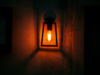 A lamp is lit up and casting a warm glow on the wall creating sense of comfort. The light is yellow and the lamp is sitting on a wall