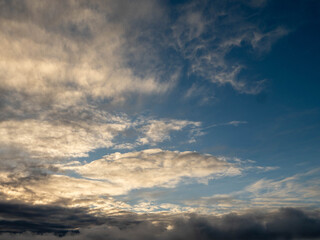 The sky is filled with fluffy clouds, and the sun is peeking through them, creating a beautiful and calming scene. The clouds are scattered throughout the sky, with some closer to the horizon