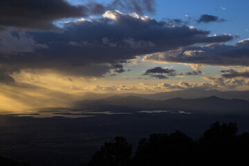 Naklejka premium Sun rays between the clouds reflecting on the mountains and the Gabriel y Galan reservoir at sunset