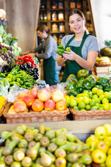Young woman in apron sells green capsicum in vegetable shop