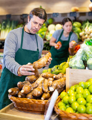 Salesman in apron offering root yucca on the supermarket