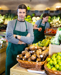 Portrait of friendly man seller in an apron against the background of fruits and vegetables in a supermarket