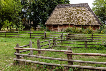 A wooden fence surrounds a small house with a thatched roof