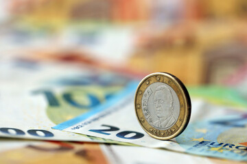 One euro coin lies on huge amount of different euro dollars banknotes