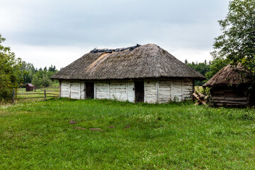 A small, old house with a thatched roof sits in a grassy field