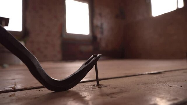 Nail puller pulls a Iron Nail out of the wooden board. Removing a Iron Nail with a nail puller from a wooden floorboard in a house.