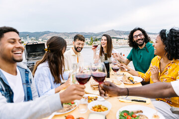 Group of young friends having dinner at home terrace. Millennial people enjoying time together sitting on table at summer party celebration. Friendship concept