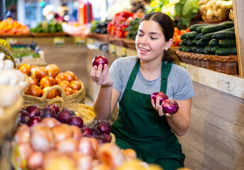 Saleswoman near fruit and vegetables stalls offering to buy red onion