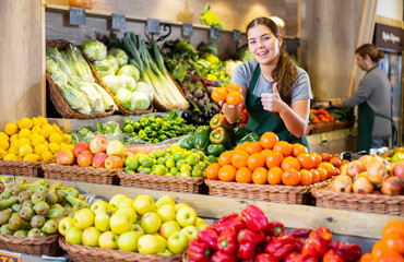 Saleswoman near fruit and vegetables stalls offering to buy mandarin oranges