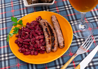 Fried red beans and sausage served on plate and decorated with greenery, traditional dish of Catalonia. Butifarra con alubias
