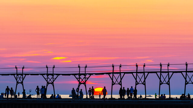 The lighthouse pier at Grand Haven, Michigan, shown in silhouette as the sun sets below the horizon - Powered by Adobe