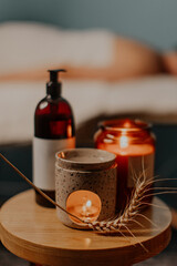 A warm, cozy image of a beautiful spa composition with an ear of wheat, a bottle of oil and candles. Blurred figures of the massage therapist and his guest in the background.