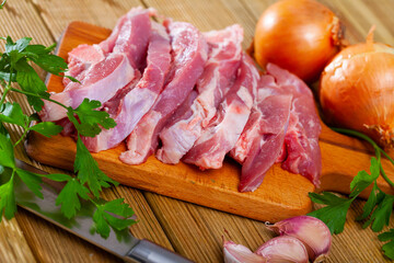Raw sliced turkey thigh on bone on wooden surface with seasonings. Dietary cooking ingredient