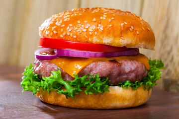 Tasty grilled beef burger with cheese, lettuce, onion, tomato served on wooden board