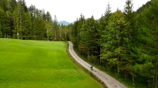 Aerial view of male cyclist riding gravel bike in September in Bavaria, Germany in forest. Drone view of bicyclist from behind riding along gravel bike route in Bavarian forest in the mountains. 