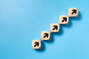 A stack of wooden blocks with arrows pointing upwards for business, sales, revenue or investment growth concept isolated on blue background