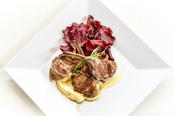 A plate of lamb chops with a side of potatoes and a sauce