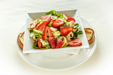 A salad with strawberries, lettuce, and mushrooms on a white plate