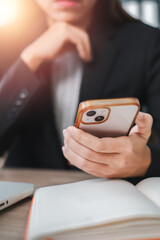 Close-up of a business professional using a smartphone at a desk with an open notebook and laptop, highlighting modern work environments.