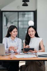 Two women engaged in a business meeting, using digital tablets in a modern office environment.
