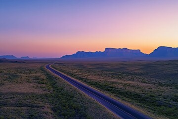 Fototapeta premium Desert road at dusk with vibrant colorful sky and distant mountains.