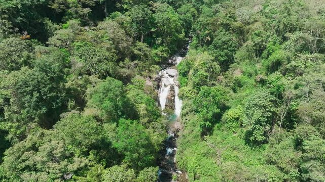 Aerial view orbits around majestic two-tiered waterfall nestled in Costa Rica's pristine rainforest in San Gerardo de Rivas. Cascading waters merge into turquoise pools as drone circles the scene.