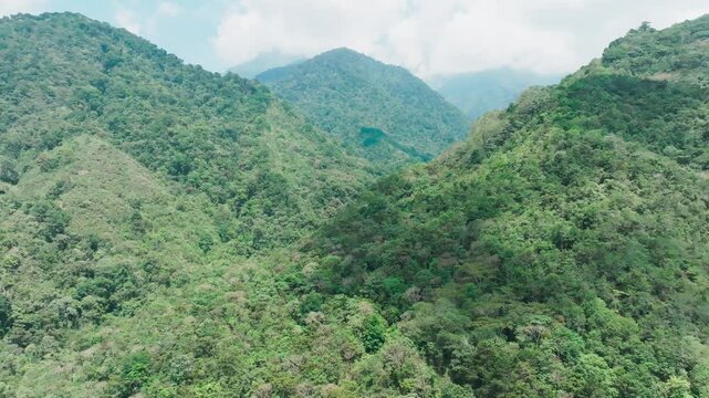 Sweeping aerial view of pristine tropical mountain ranges carpeted in dense rainforest in San Gerardo de Rivas, Costa Rica. Misty clouds drift between verdant peaks as camera glides backwards.