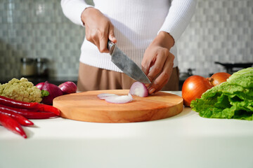 Selective focus on woman's hand chopping onion on cutting board