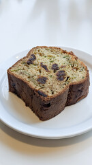 Zucchini bread slice on a white plate, surrounded by greenery. Perfect for brunch. Concept of brunch, bread, zucchini, plate, greenery, dessert, snack
