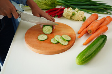 Selective focus on woman's hand chopping cucumber on cutting board