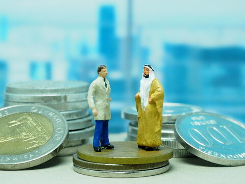 Mini toy of action figure at outdoor with blurred background. Toy photography concept design. Businessman and arabian man talking business with many coin.
