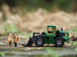 Mini toy of action figure at table with blurred background. Business photography concept design. Minifigure of engineer character with tractor at site plant.