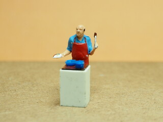 Naklejka premium Mini toy of action figure at with blurred background. Miniature photography concept design. Minifigure of chef character cooking at kitchen.