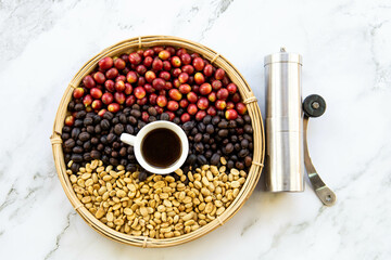 coffee cherries, roasted coffee beans, and green coffee beans in a basket with manual coffee grinder