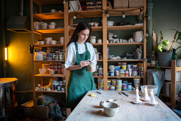Concentrated woman potter connecting handle to clay mug for secure material bonding, preparing...