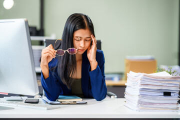 A businesswoman sits at her desk in a modern office, surrounded by numerous documents. She works...