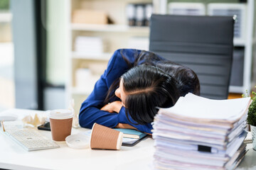 A businesswoman sits at her desk in a modern office, surrounded by numerous documents. She works...