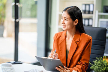 A beautiful Asian businesswoman works at her desk, exuding professionalism and focus.She is deeply...
