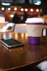 A Coffee Cup placed on a Table featuring a Smartphone in a Cozy Cafe Setting that feels inviting