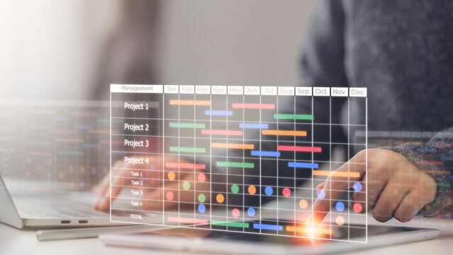 A project manager working on laptop and updating tasks and milestones progress planning with a Gantt chart scheduling interface for the company on a virtual screen. Business Project Management System