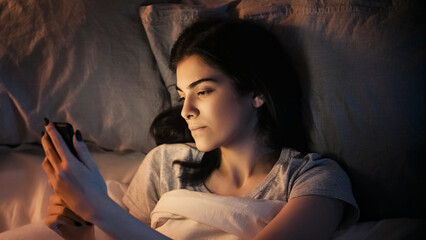 Mobile night. Gadget insomnia. Relaxed sleepy bored woman using phone app online scrolling feed in bed late in dark home bedroom.