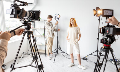 Behind scene. Female posing. Team work on preparing studio equipment work. Video operator photographer model lighting set up shooting.