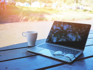 White cup of coffee and blank screen laptop computer with glasses on table on holiday vacation.