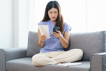 Asian woman holding paper document calculating money savings paying bills in mobile application using smart phone payment online with paying household bills tax insurance managing budget.