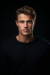 Fototapeta premium Close-up portrait of an elegant young European man with expressive blue eyes, confident gaze, short smooth haircut, light brown hair, dark sweater, high-quality RAW image with dark background