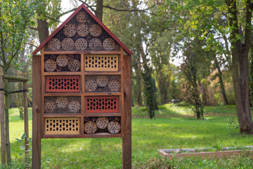 A handcrafted insect hotel in a lush green park, surrounded by trees, offers a glimpse into sustainable wildlife habitats. Perfect for projects on biodiversity, gardening, or eco-tourism.