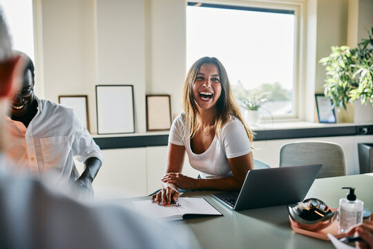Diverse Cheerful Team Meeting With Smiling Professionals in Bright Office Setting. A woman laughs loudly at a piece of good news her colleagues have told her