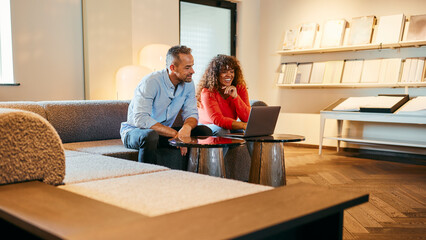 Couple Enjoying Quality Time Together in a Cozy Living Room Setting. They are sitting smiling and watching something funny on their laptop. The woman is wearing an orange shirt