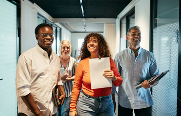 Diverse Group of Professionals Walking and Smiling in Office Corridor. They have just left a meeting and are all walking away happily with notebooks in their hands